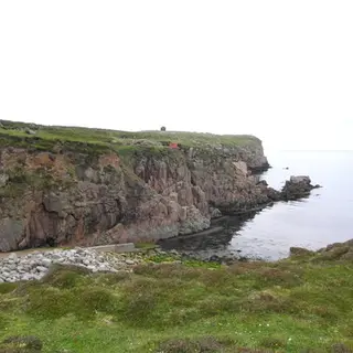 The red cliffs and shingle shore of Tory Island under a pale sky