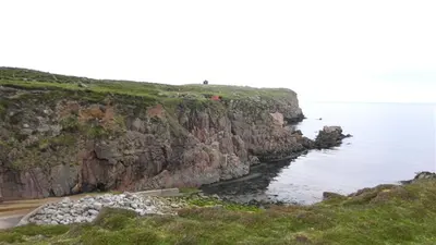 The red cliffs and shingle shore of Tory Island under a pale sky