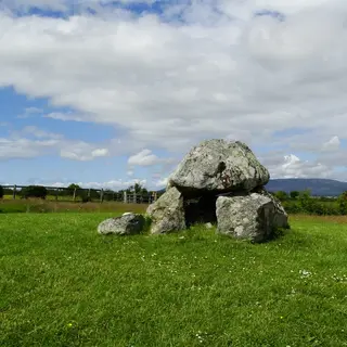 A dolmen of grey boulders in the open field at Carrowmore, with hills beyond