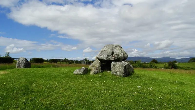 A dolmen of grey boulders in the open field at Carrowmore, with hills beyond