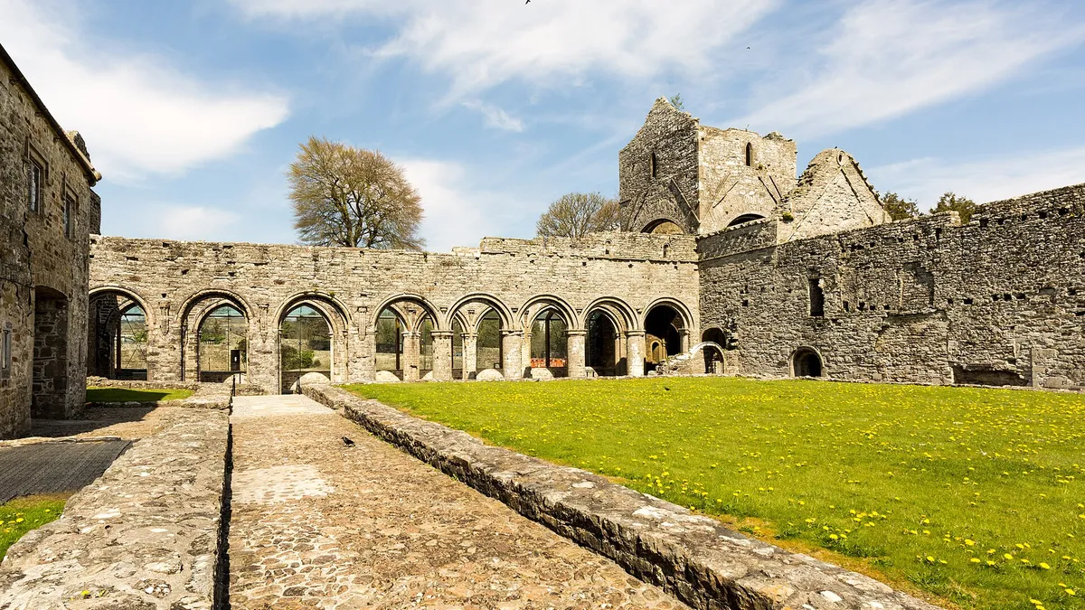 The cloister of Boyle Abbey with its round arches and the tower behind