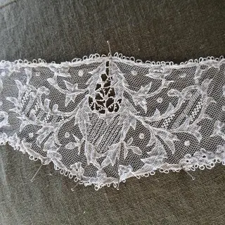 A piece of Carrickmacross lace laid out flat with its needle beside it