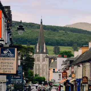 Shop signs on a Kenmare street with the church spire behind them