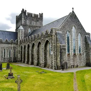 The stone front and buttresses of St Brigid's Cathedral in Kildare town above its graveyard