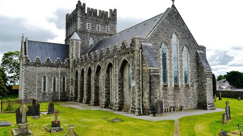 The stone front and buttresses of St Brigid's Cathedral in Kildare town above its graveyard