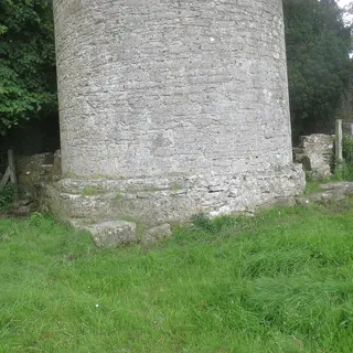 The base of the round tower at Kilree with the church ruin beside it in long grass