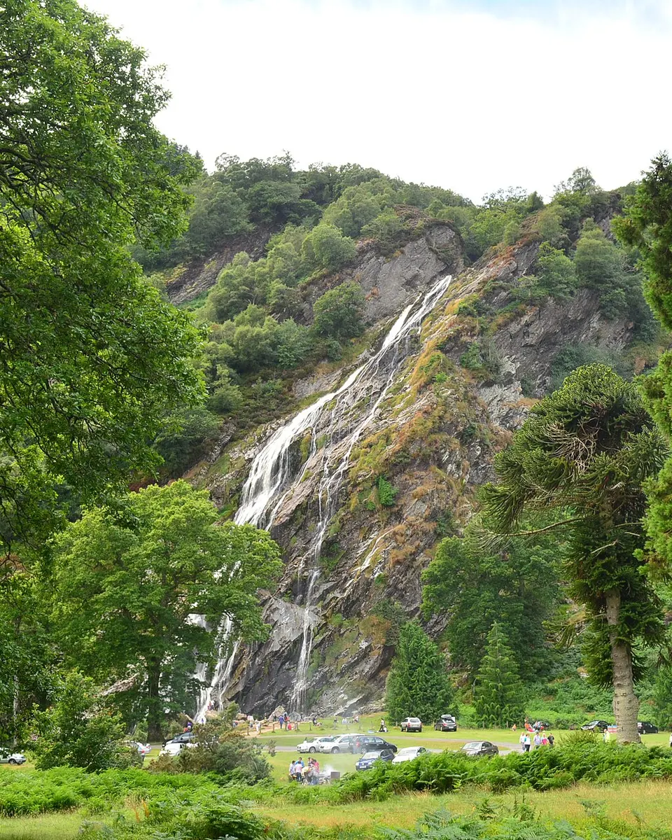 Powerscourt Waterfall falling down the wooded hillside to the grass below