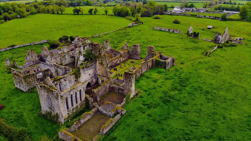 Athassel Abbey from the air, the whole ruin laid out in a green field beside the river