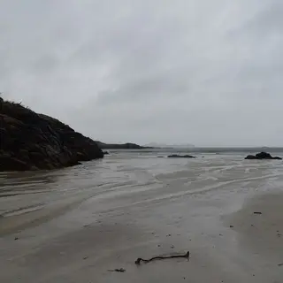 Wet sand and a headland at Carrickfinn Beach under a grey sky