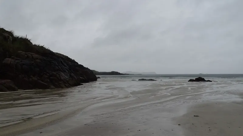 Wet sand and a headland at Carrickfinn Beach under a grey sky