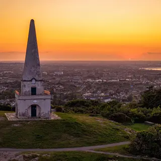 The obelisk on Killiney Hill with the bay below it at sunset