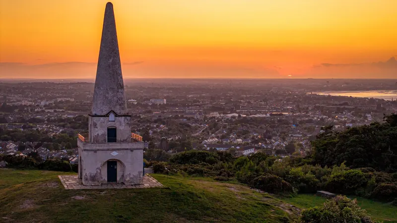 The obelisk on Killiney Hill with the bay below it at sunset