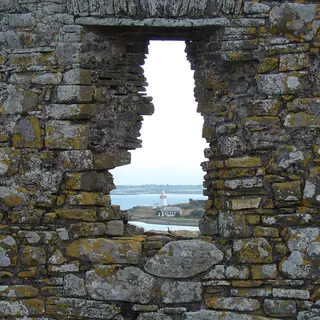Scattery Island and its round tower seen through a gap in a ruined wall across the Shannon estuary