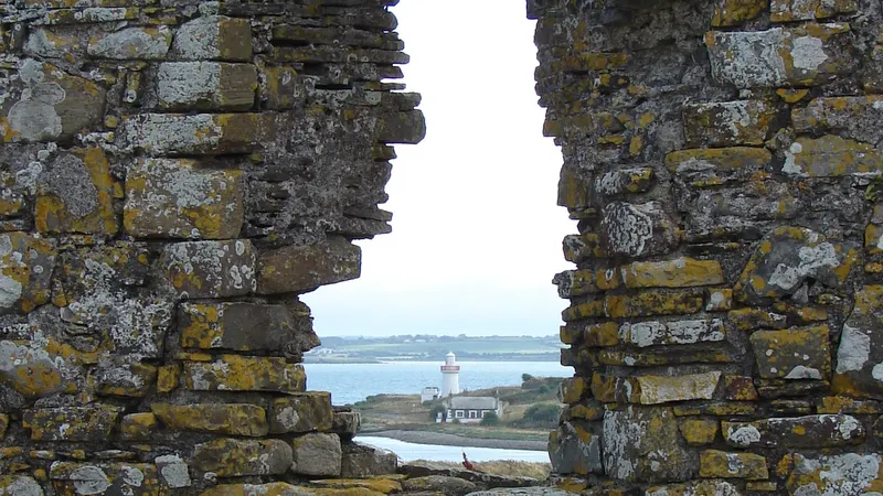 Scattery Island and its round tower seen through a gap in a ruined wall across the Shannon estuary