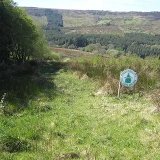A waymarker standing in rough grass on the Miner's Way above the valley