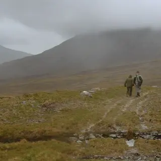Two walkers on a bog track in Wild Nephin National Park with the hills in cloud behind them