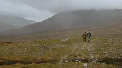 Two walkers on a bog track in Wild Nephin National Park with the hills in cloud behind them