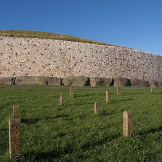 The white quartz front and kerbstones of the Newgrange mound above green fields