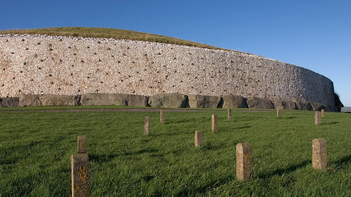 The white quartz front and kerbstones of the Newgrange mound above green fields