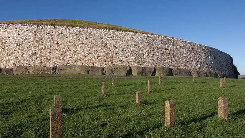 The white quartz front and kerbstones of the Newgrange mound above green fields