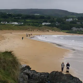 Walkers on the long strand at Culdaff with houses on the hill behind