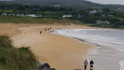 Walkers on the long strand at Culdaff with houses on the hill behind