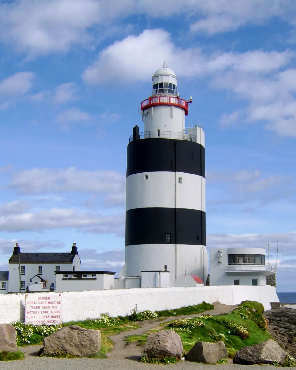 The black and white banded tower of Hook Lighthouse against a blue sky